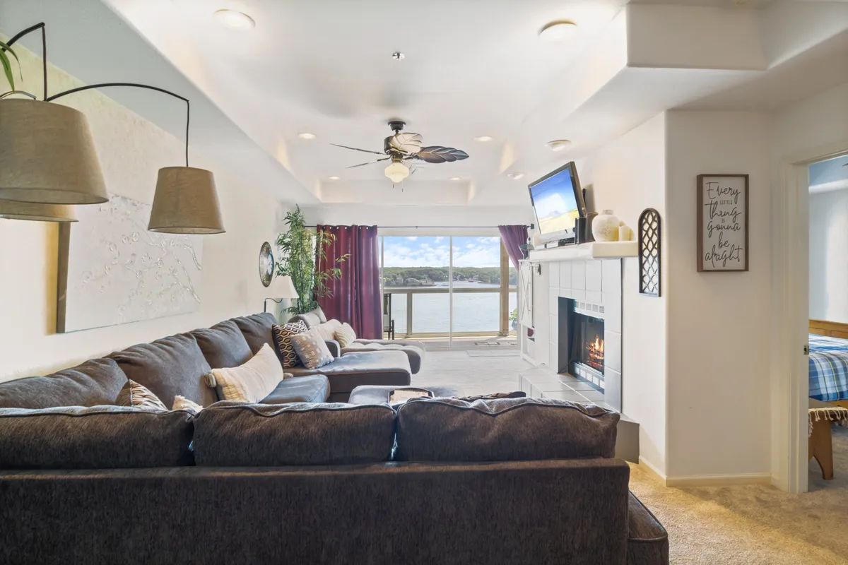 The photo captures a warm and inviting living area featuring another large sectional sofa, a fireplace, a television, and expansive windows that showcase a breathtaking sunset over the lake. The setup is perfect for movie nights, family gatherings, or simply enjoying the lakeside ambiance.
