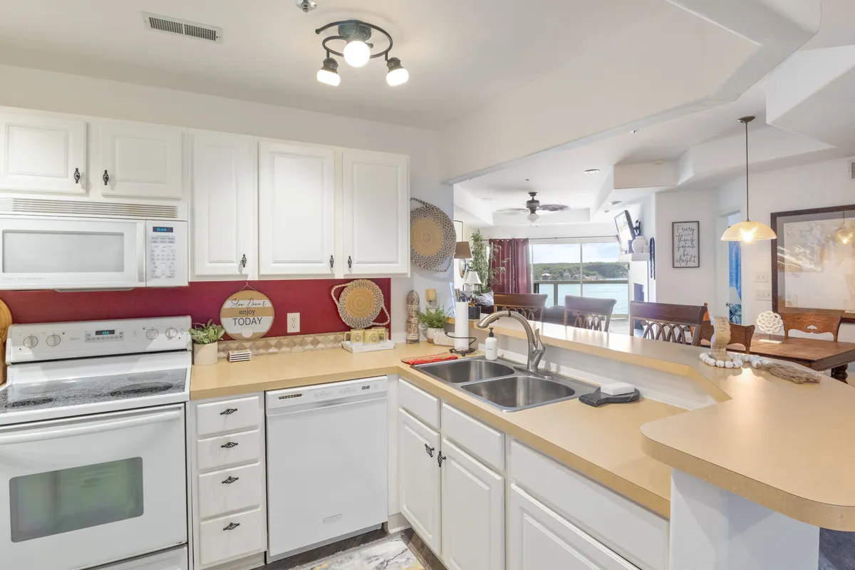 A cheerful, well-lit kitchen featuring a spacious countertop, modern sink, various appliances, and a striking red accent wall. Decorative items add personality, and ample space around the counter suggests it's ideal for cooking and entertaining.