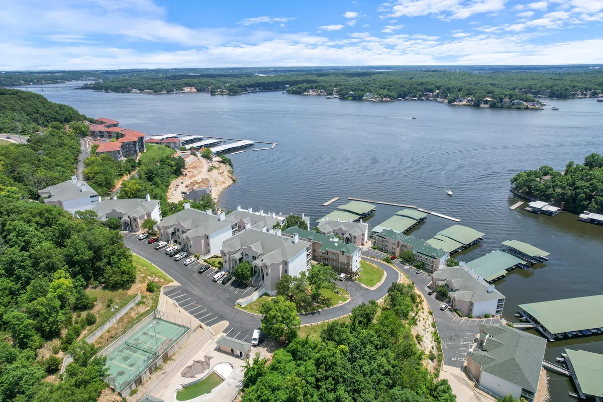A serene lake view features boathouses along the shore, lush greenery, and residential buildings tucked into the landscape. The presence of docks and boat slips suggests opportunities for boating, fishing, and relaxing by the water.