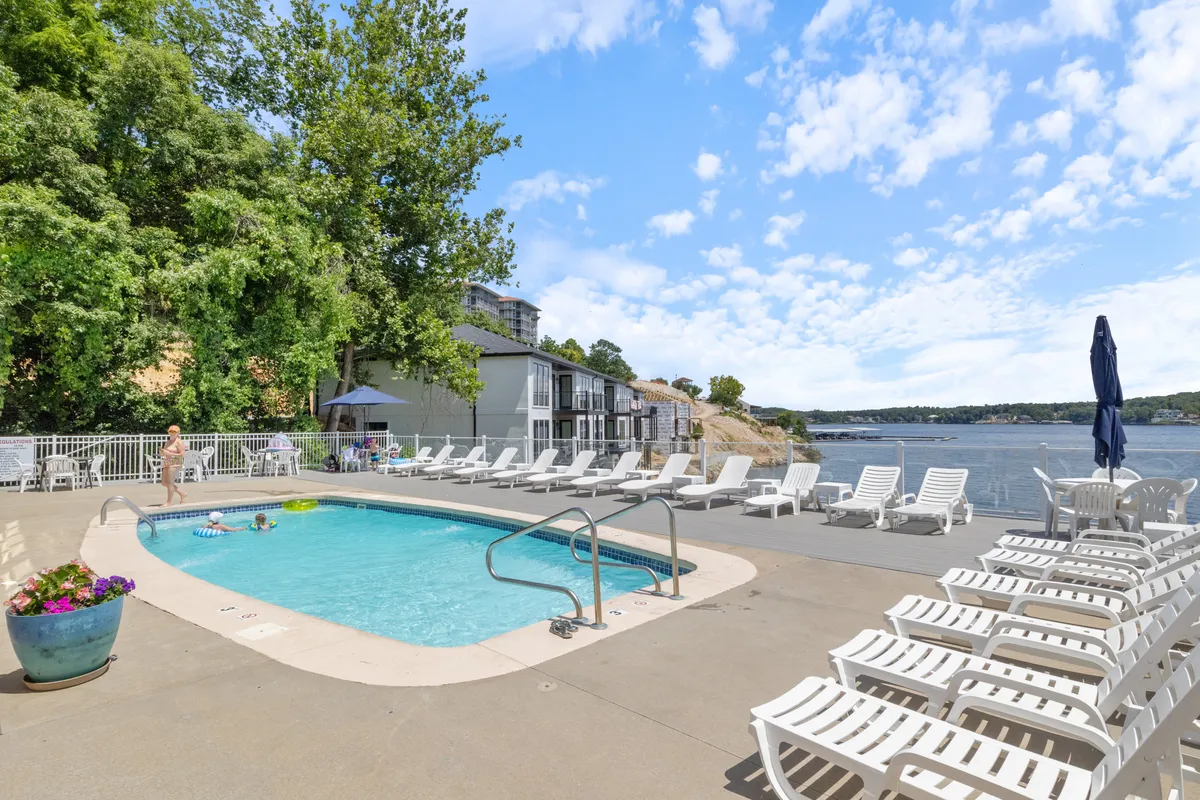 A stunning outdoor swimming pool is framed by comfortable lounge chairs, with a beautiful waterfront view stretching into the distance. The setting invites guests to swim, sunbathe, and gather socially around the pool, all while enjoying the relaxing ambiance of the water nearby.