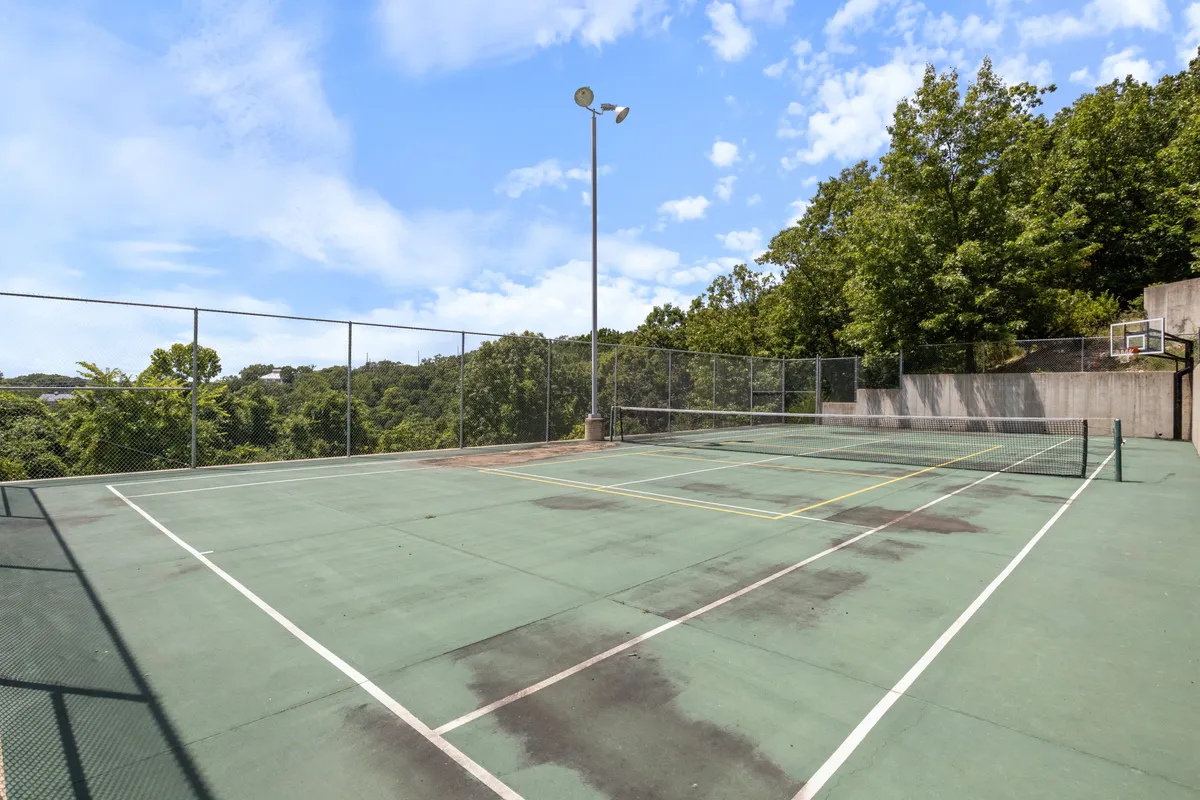 An energetic exterior scene featuring a tennis court and basketball hoop, surrounded by mature trees. The setting encourages active recreation, with opportunities for friendly matches and sporting fun under the sun.