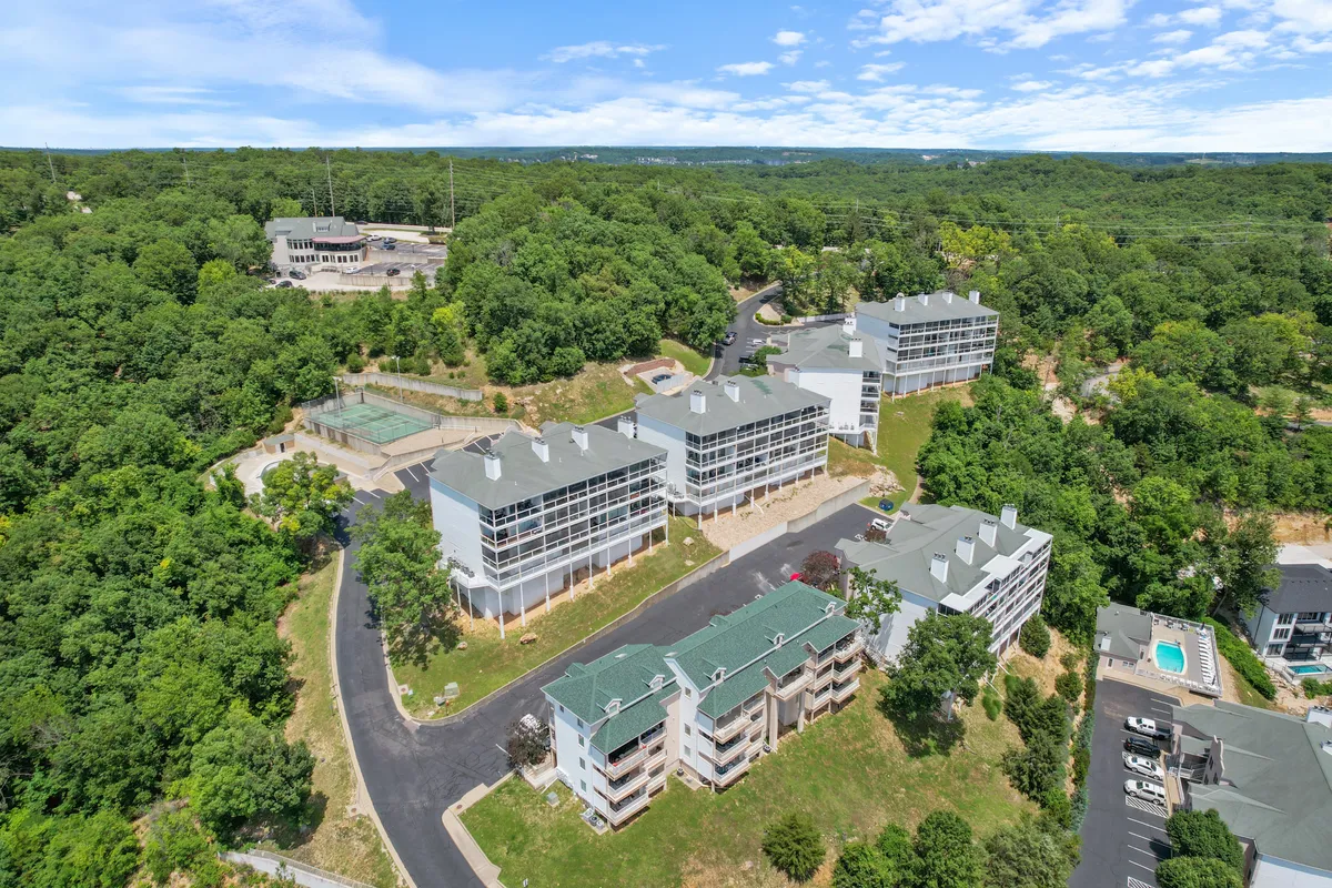 A wide exterior shot featuring multiple buildings, lush greenery, a swimming pool, and a tennis court. The image suggests a vibrant, activity-filled atmosphere suitable for groups and retreats.
