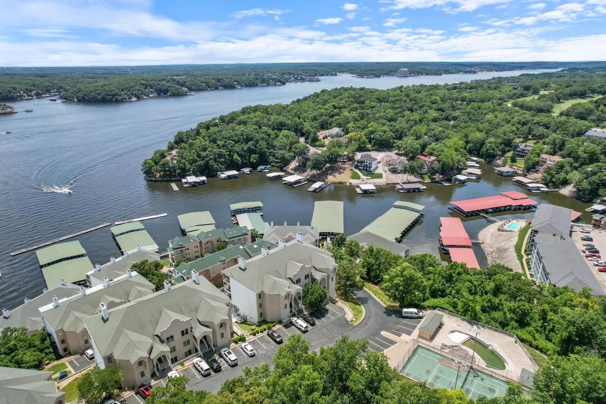 A sweeping view of the waterfront area at Lake of the Ozarks, showcasing marinas lined with boats, lush greenery embracing the shoreline, and residential buildings nestled nearby. The scene is filled with opportunities for boating, fishing, swimming, and picnicking, with the lake taking center stage as a hub for recreation and relaxation.