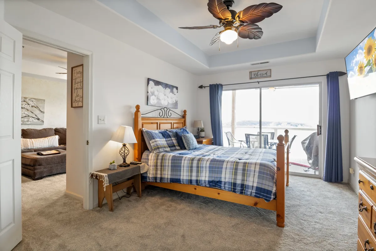 A tranquil bedroom with a neatly made bed, a sliding glass door opening to scenic views, tasteful art, and a cozy lamp. The space exudes serenity and comfort, ideal for relaxation or enjoying the morning light.