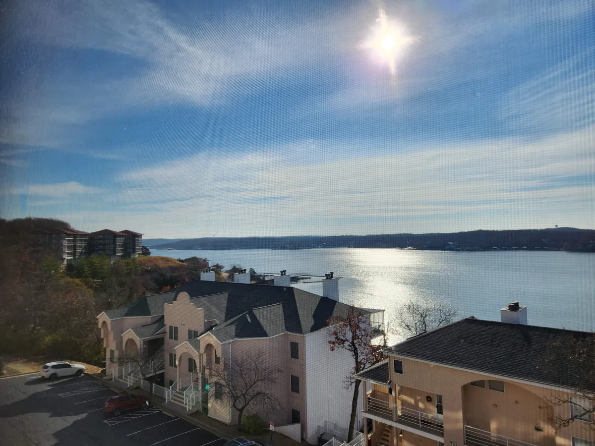 This view image captures the tranquil lake with sunlight reflecting off the water, surrounded by buildings that blend into the landscape. The scene suggests a peaceful environment ideal for boating, fishing, or enjoying sunrise and sunset by the water.