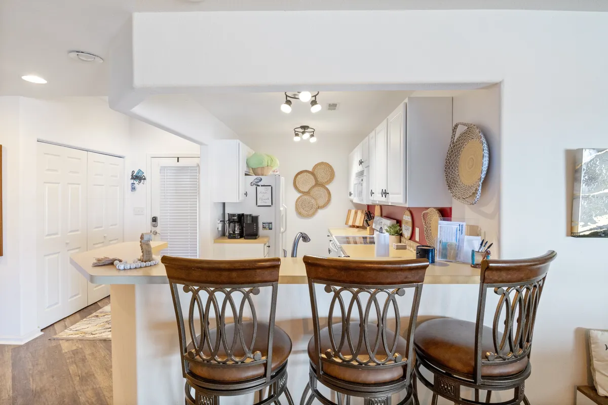 A bright, stylish open kitchen with a spacious countertop, bar stools for casual seating, modern cabinetry, and playful decorative plates. The layout encourages socializing and seamlessly connects to the living and dining areas, ideal for hosting meals and gatherings.