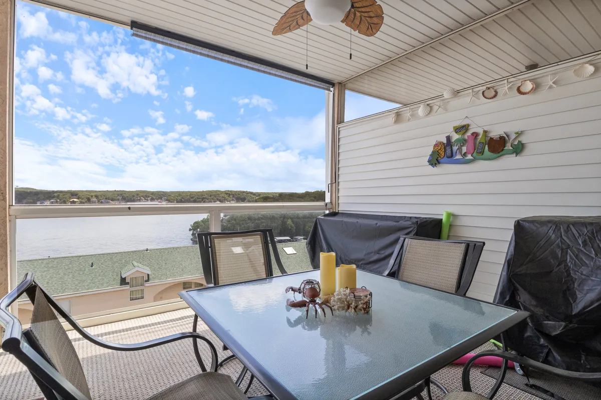 An exterior shot featuring a table with a glass top and decorative candles, positioned to take advantage of a serene view of the lake and surrounding landscape. The setup invites guests to enjoy meals or drinks outdoors while watching the water.